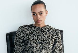 Zara model wearing cheetah-print coat and sitting on black chair.