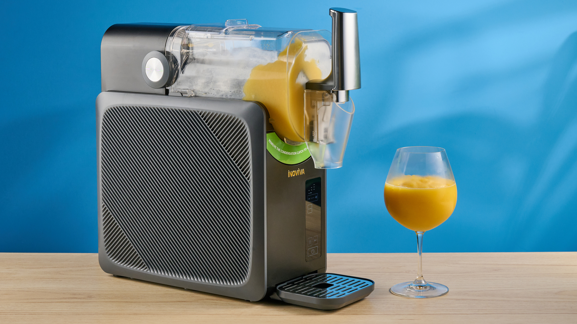 the inoviva slushie machine, a slushie maker with a plastic cylinder body, a dispensing spout, photographed making orange juice slush against a blue tom&#039;s guide background