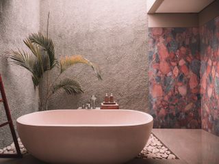 An outdoor spa bathroom with a blush bath and a marble wall featuring pink, red and gray shades