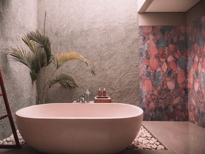 An example of spa bathroom ideas showing an outdoor bathroom with a blush bath and a marble wall featuring pink, red and gray shades