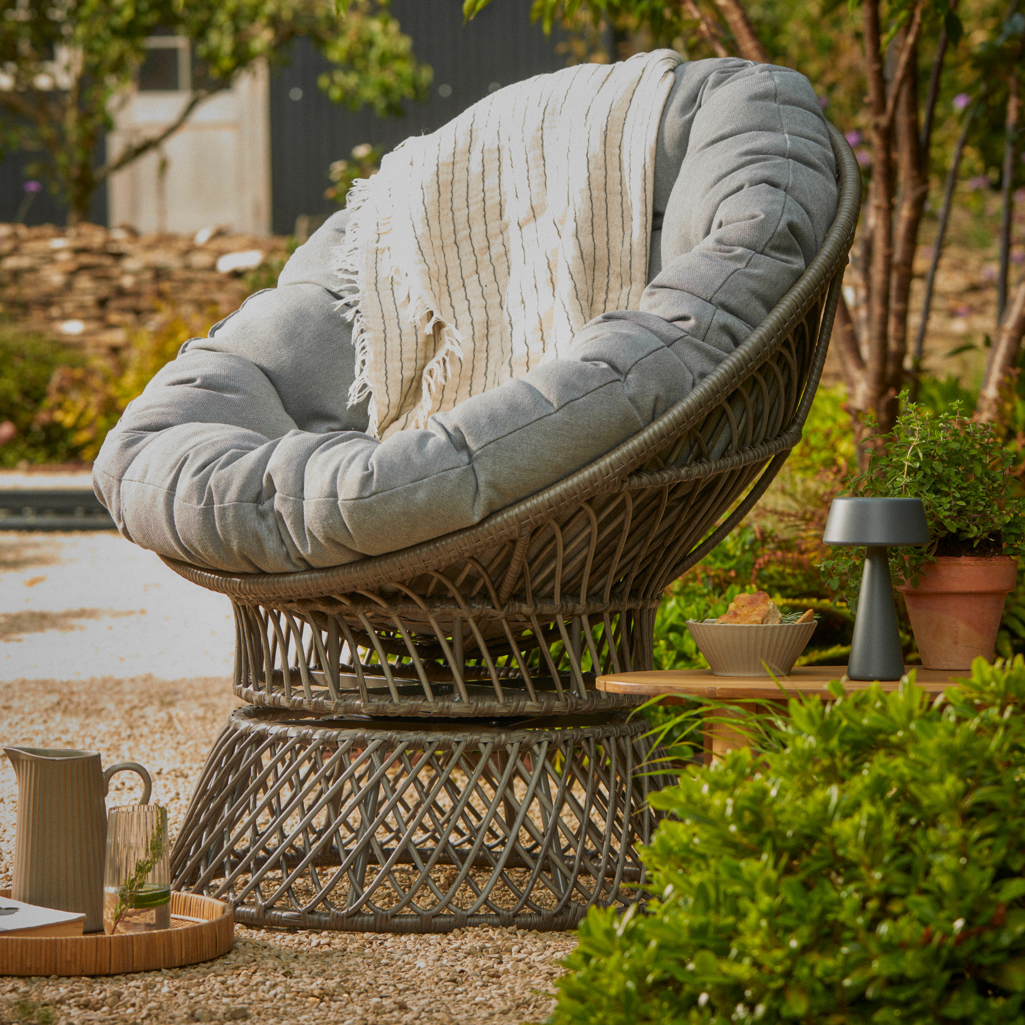 A garden swivel chair with seat cushion on a gravel floor outside