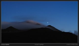 A bright star shines in a dim blue sky over a series of mountains shrouded in fog.