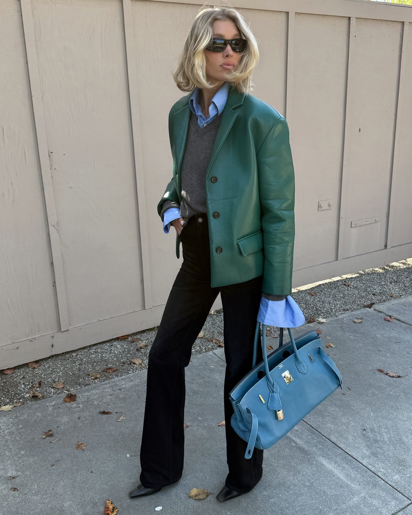 Elsa Hosk wearing a green Helsa leather jacket with a gray sweater, black pants, and a blue Hermes bag.