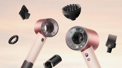 A product shot of the new Dyson Supersonic Travel, alongside the original Supersonic hair dryer, to demonstrate their size difference, and surrounded by the latter's attachment/ on a sunset cloud background