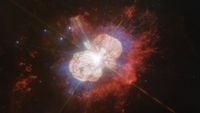 two large lobes of colorful gas radiate outward from a bright pinpoint of light 