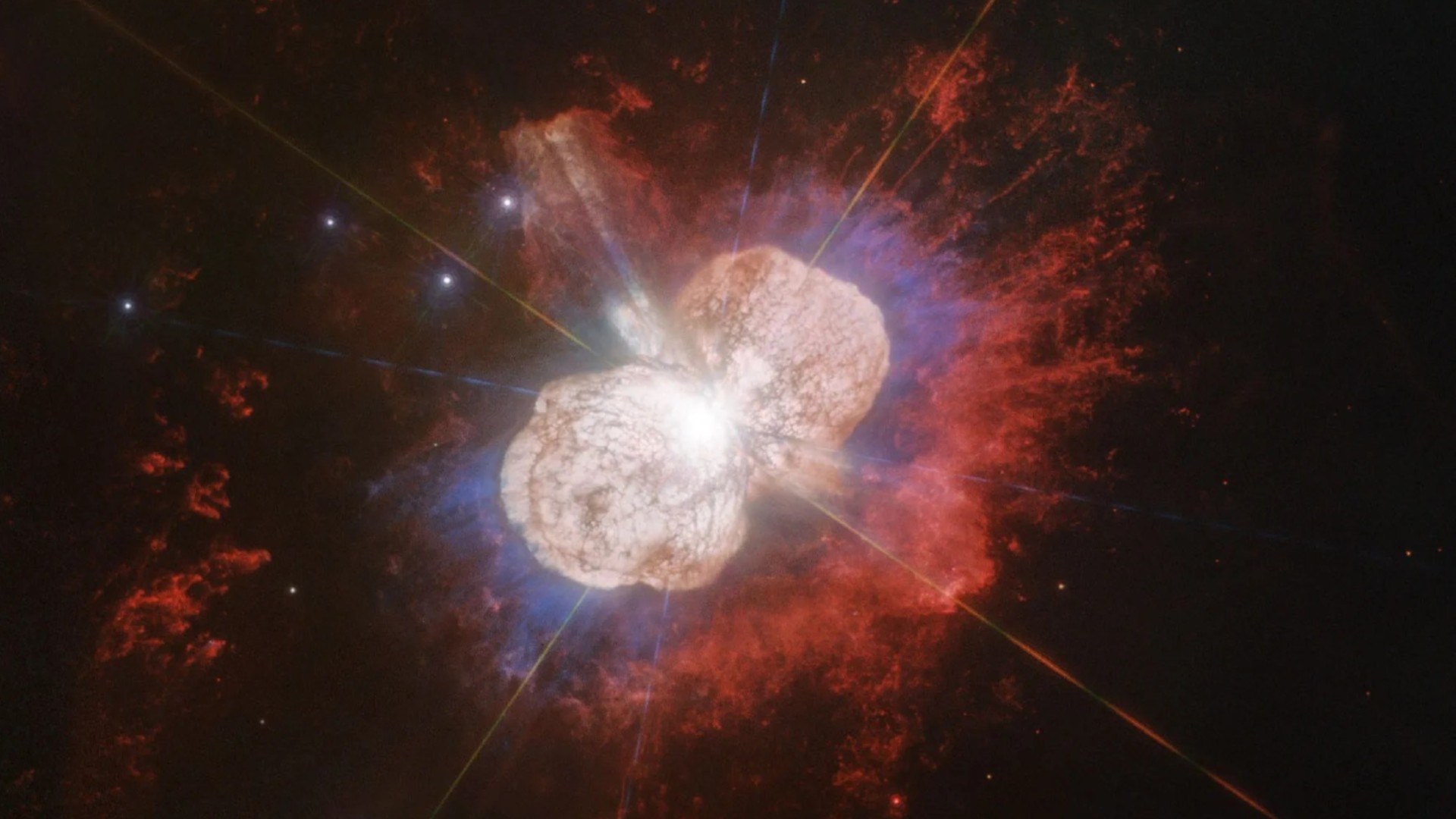 two large lobes of colorful gas radiate outward from a bright pinpoint of light 