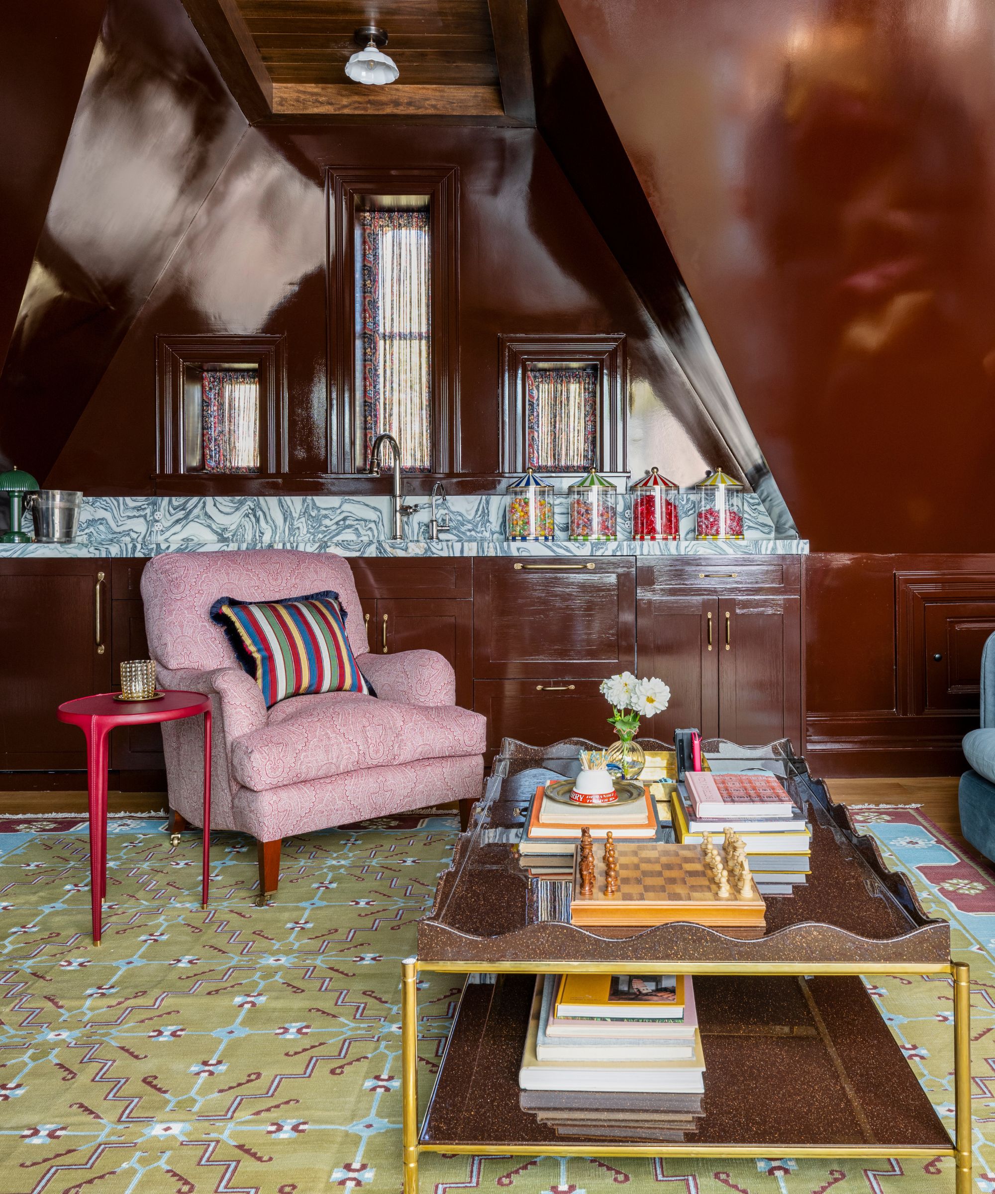 a top floor lounge in a brownstone home with glossy brown walls and cabinetry, a small kitchenette, and a layered lounge area