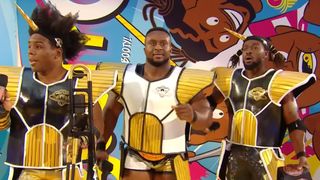 Xavier Woods, Big E, and Kofi Kingston at WrestleMania in Dragon Ball inspired Saiyan armor. Kofi and Xavier are wearing black suits, and Big E is wearing white in the center. 