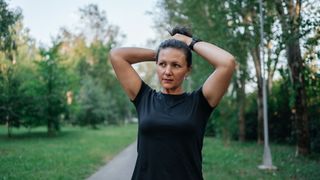 Woman tying hair back on an empty path in a park, preparing to go running