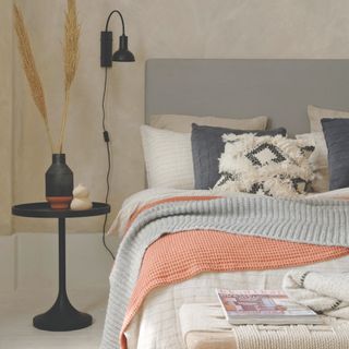 tiny guest room ideas, cream bedroom with grey bed, white painted floor, black side table and wall light, textured bedding, knitted throws, textured cushions, pampas
