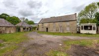 A brick farmhouse with external cladding and two neighbouring stone cottages