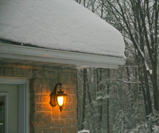 Exterior wall light in winter. The roof is covered in snow and bare trees in background are snow covered