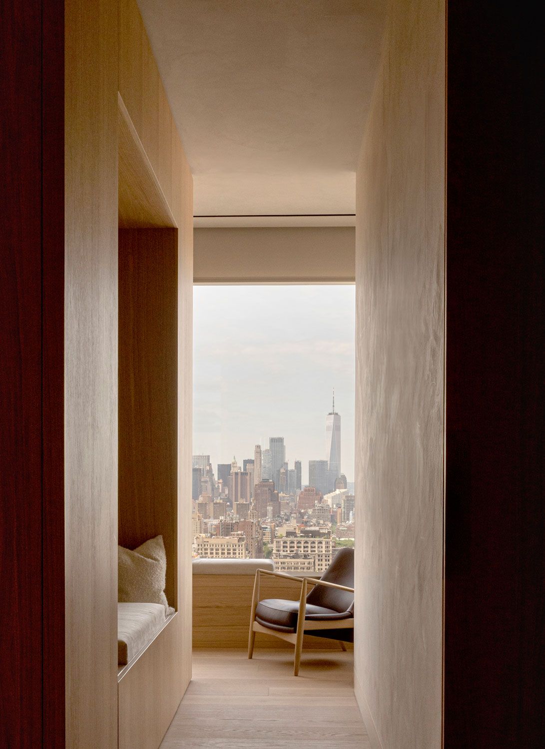 A narrow passage with built-in oak seating frames a view across Manhattan towards One World Trade Center at 262 Fifth Avenue