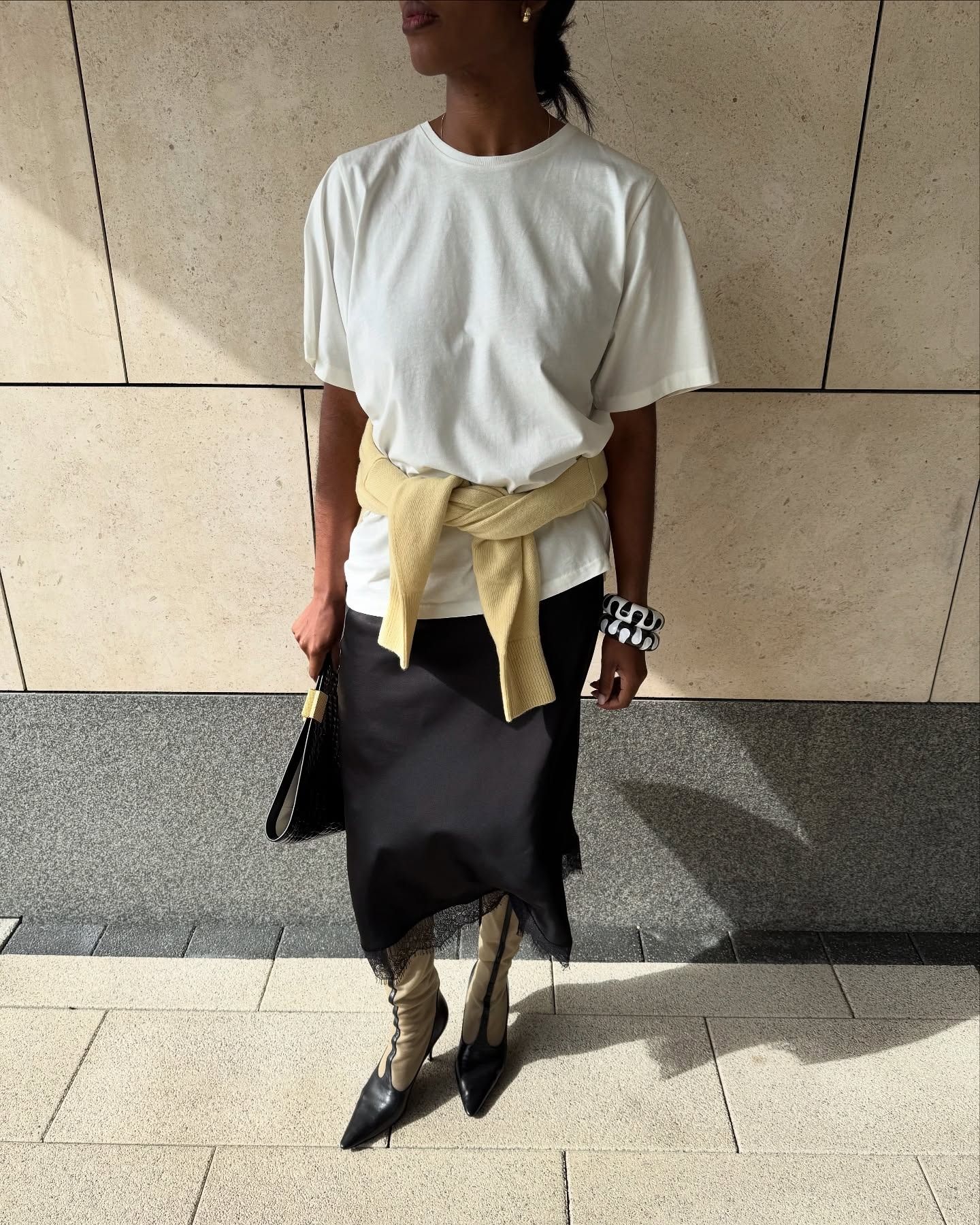 @nlmarilyn wearing a white tee, black skirt, knee-high boots, and a yellow sweater.