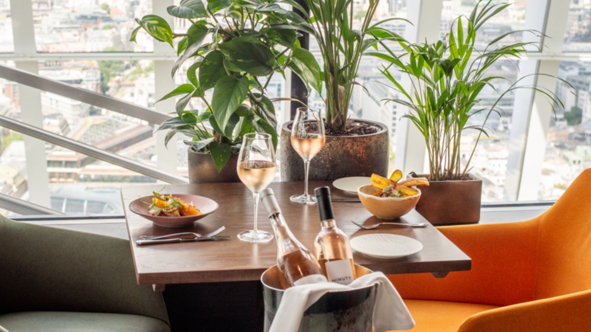 a table overlooking London at Fenchurch restaurant, with two plates of food and a bucket with two bottles of rose wine