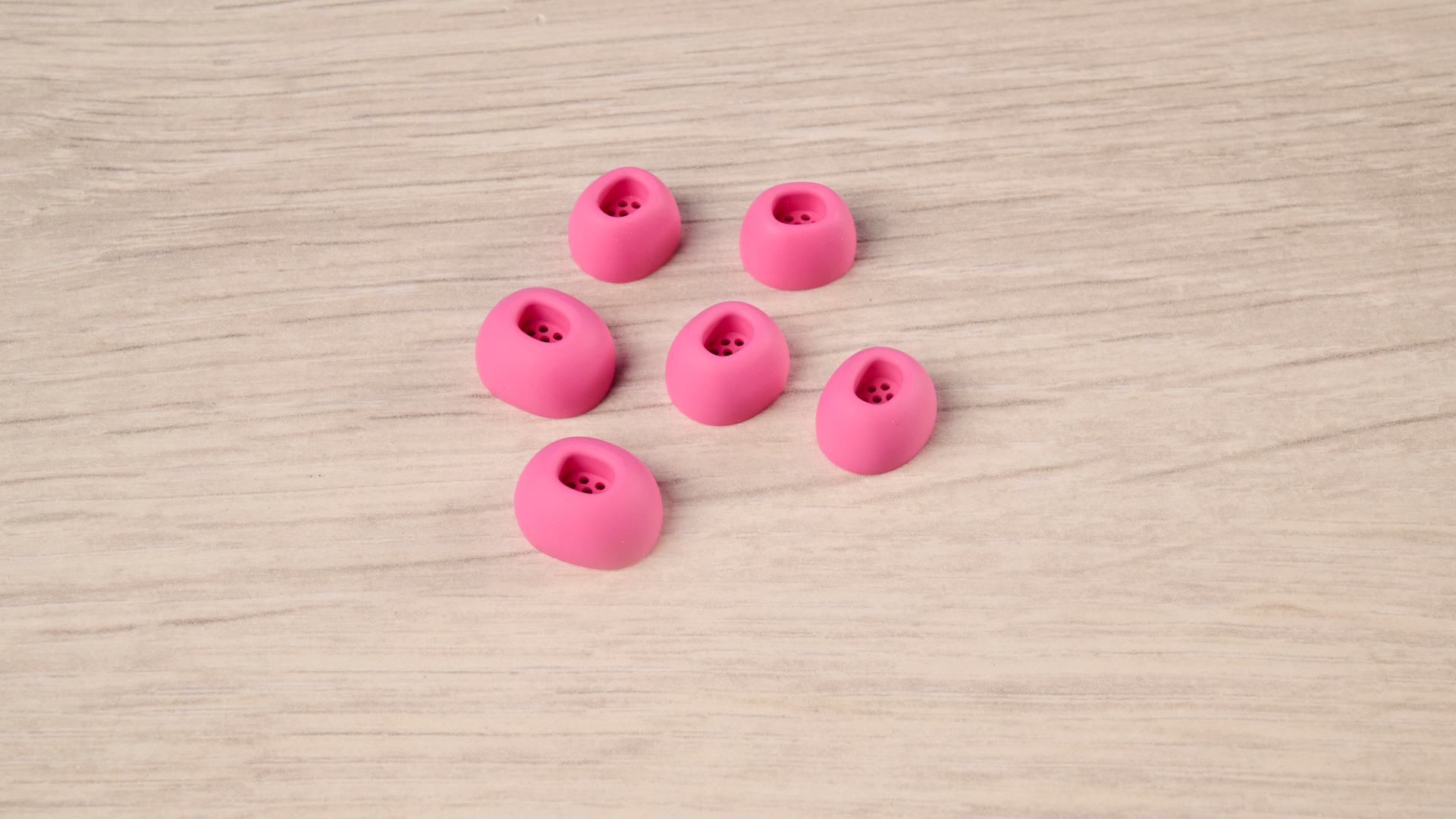 The Nothing Earbuds (3a) in pink, on a wooden surface