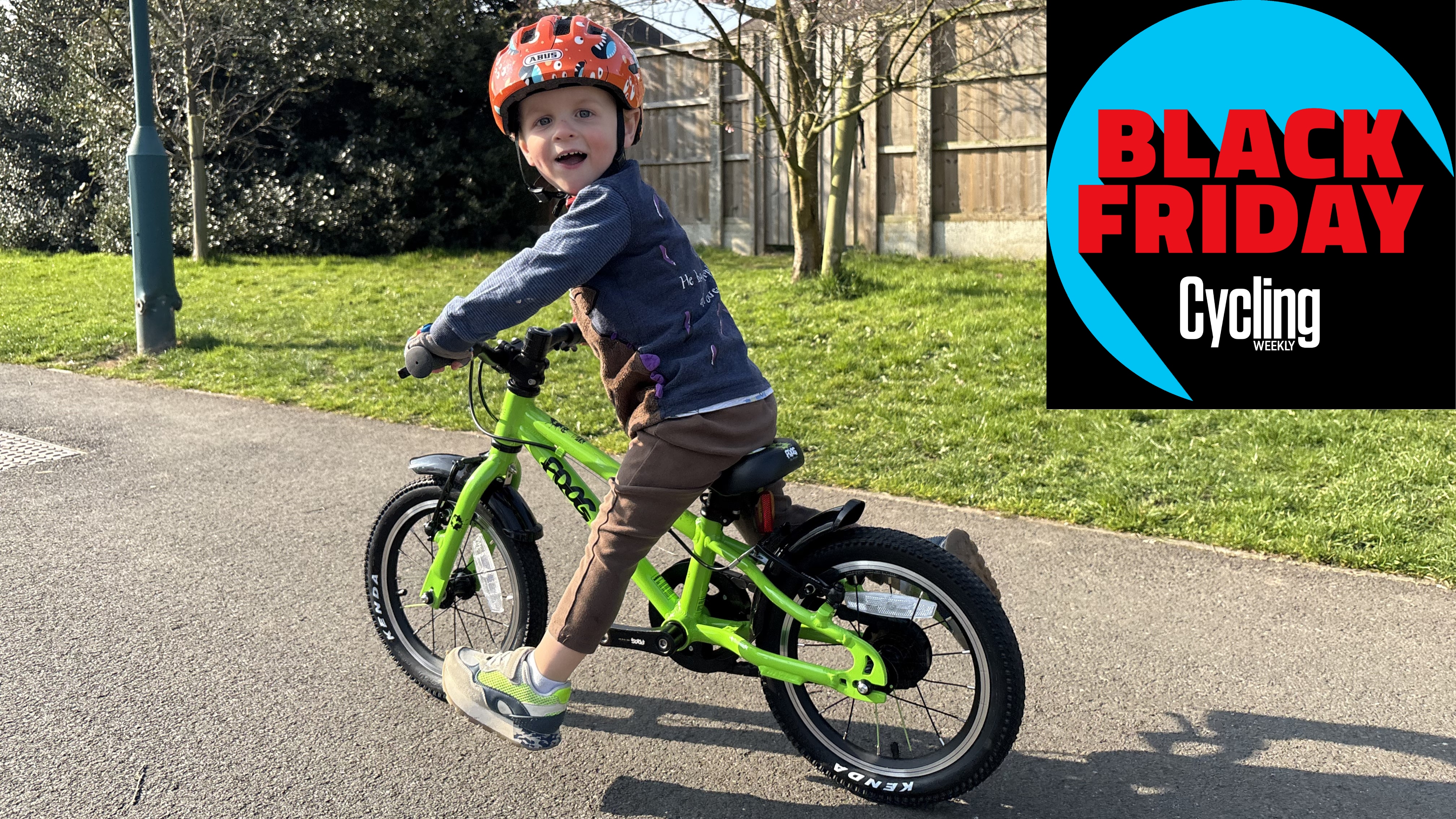 Small boy scoots on pedal bike whilst turning round to look at the camera