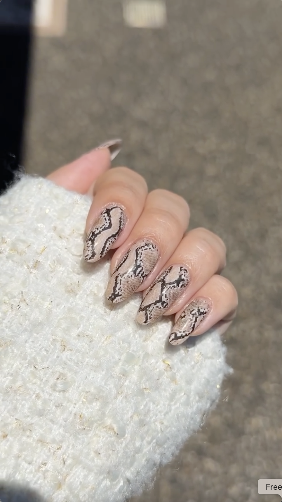 Close-up photo of a person&amp;rsquo;s hands showcasing a snakeskin print manicure on almond nails.