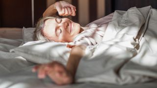 Woman stretching arm out, relaxed and comfortable in bed after sleeping with pillow between legs