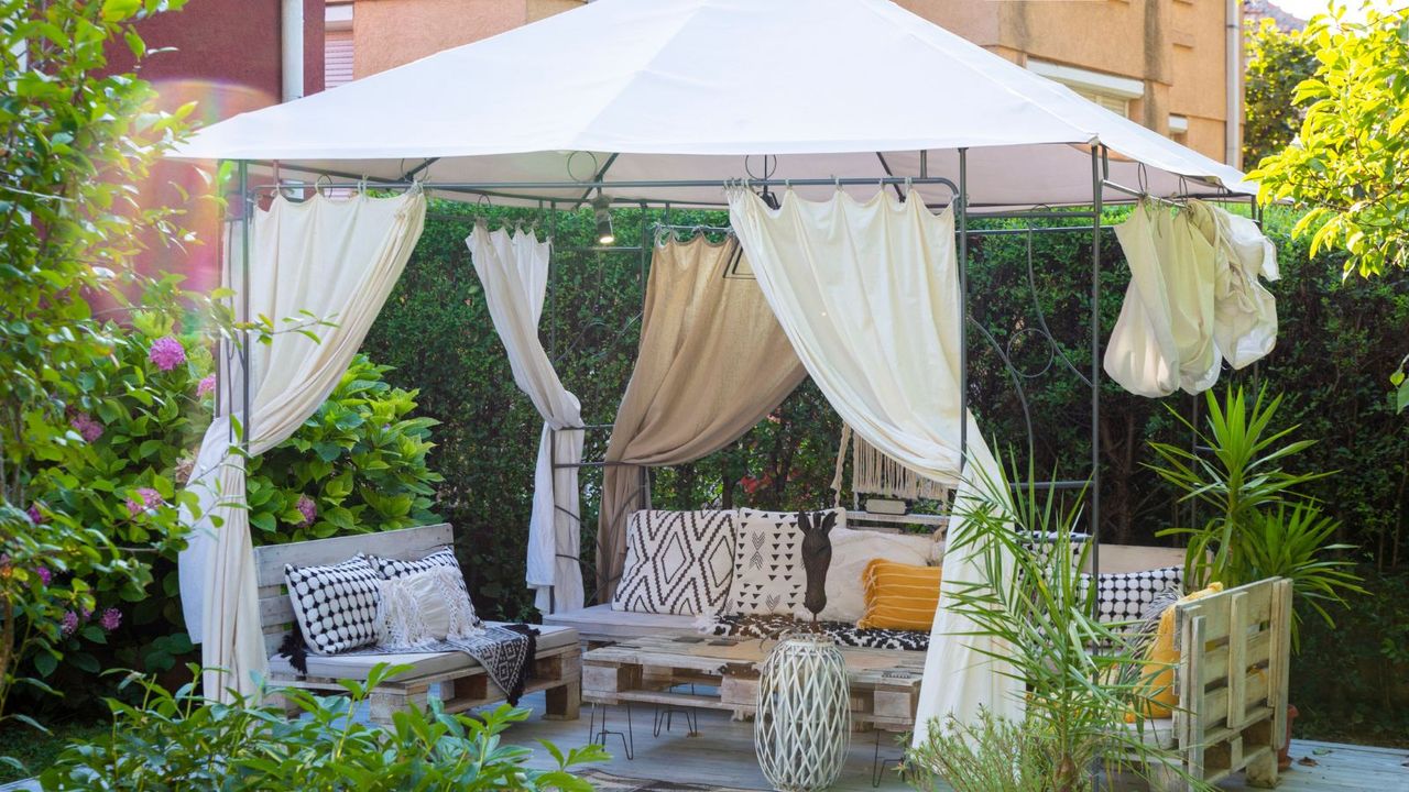 A white gazebo with white wooden sofas on a patio