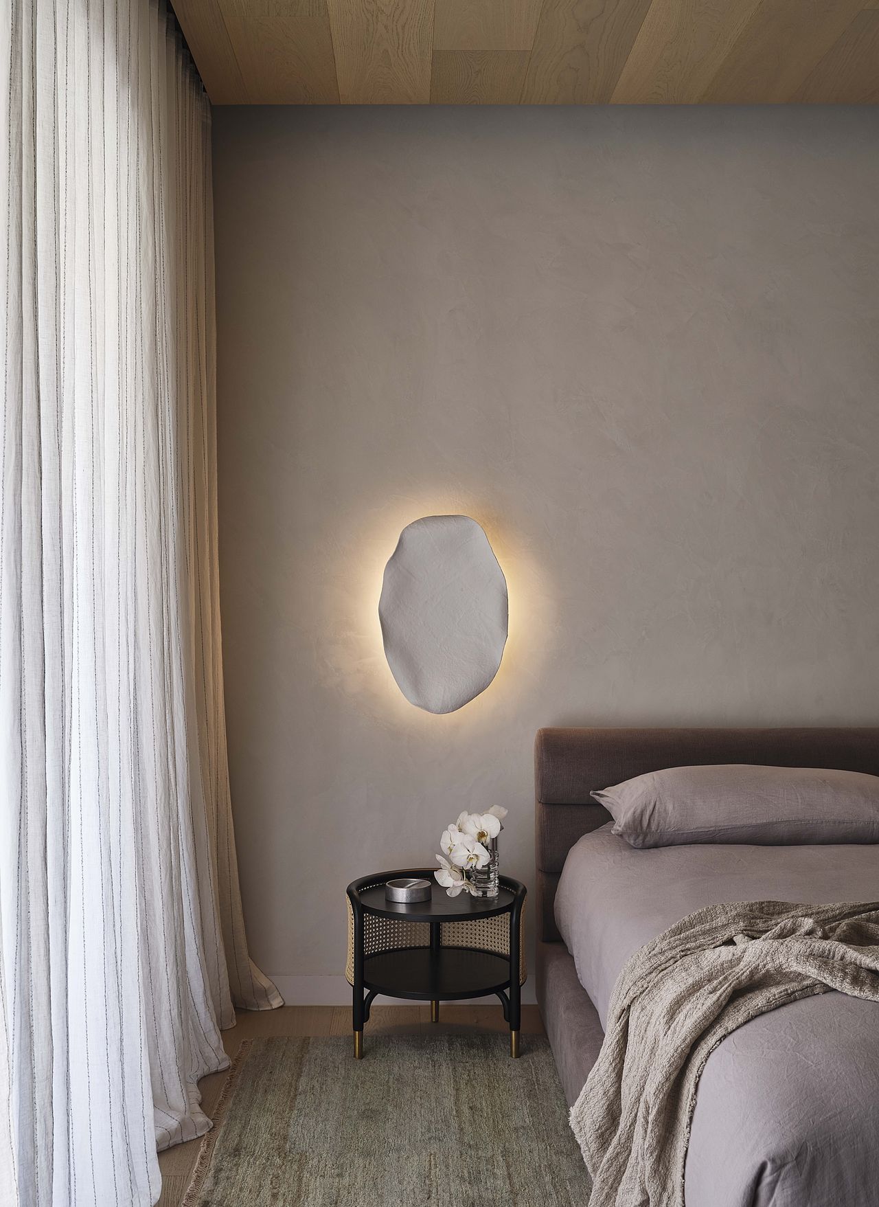 A sculptural light fixture hands above a pruple bed frame