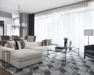 Living room with sectional in neutral, glass coffee table, and gray geometric patterned rug