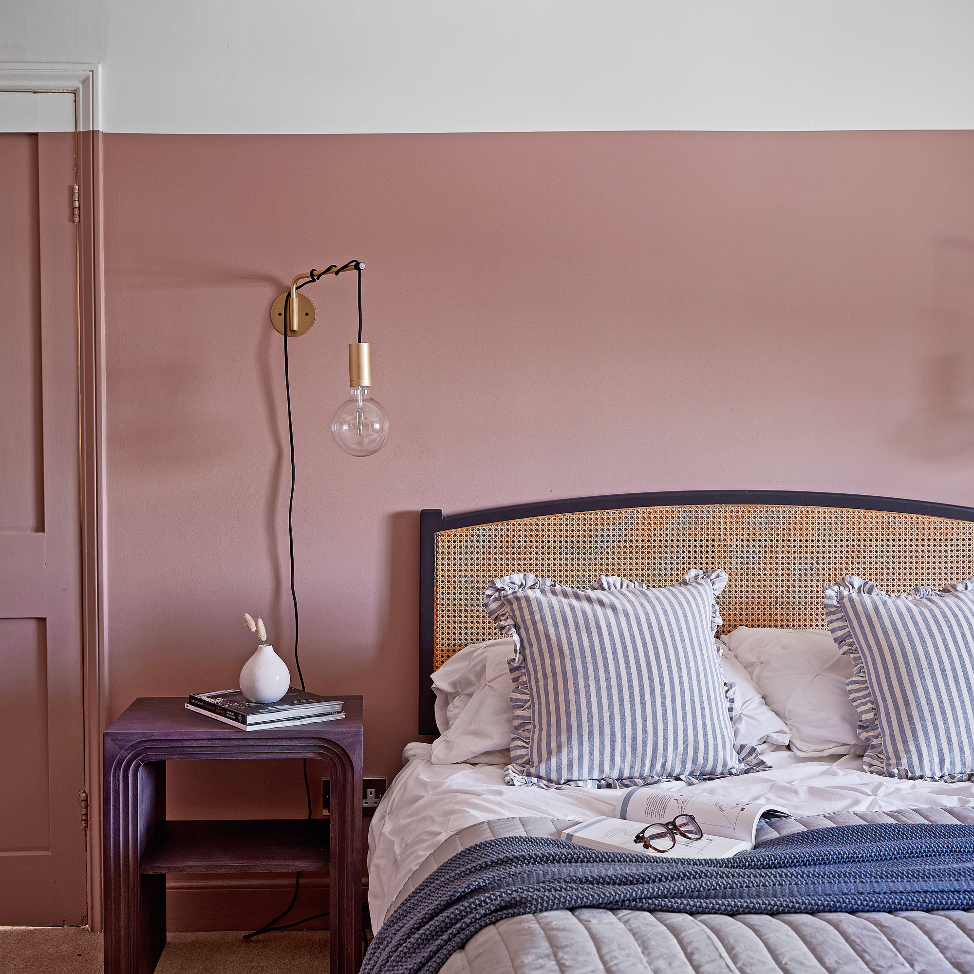 a pink and white colour drenched bedroom with a rattan headboard and globe wall light