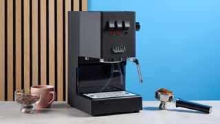 The Gaggia Classic E24 Evo Pro and its accessories on a stone surface and against a blue background