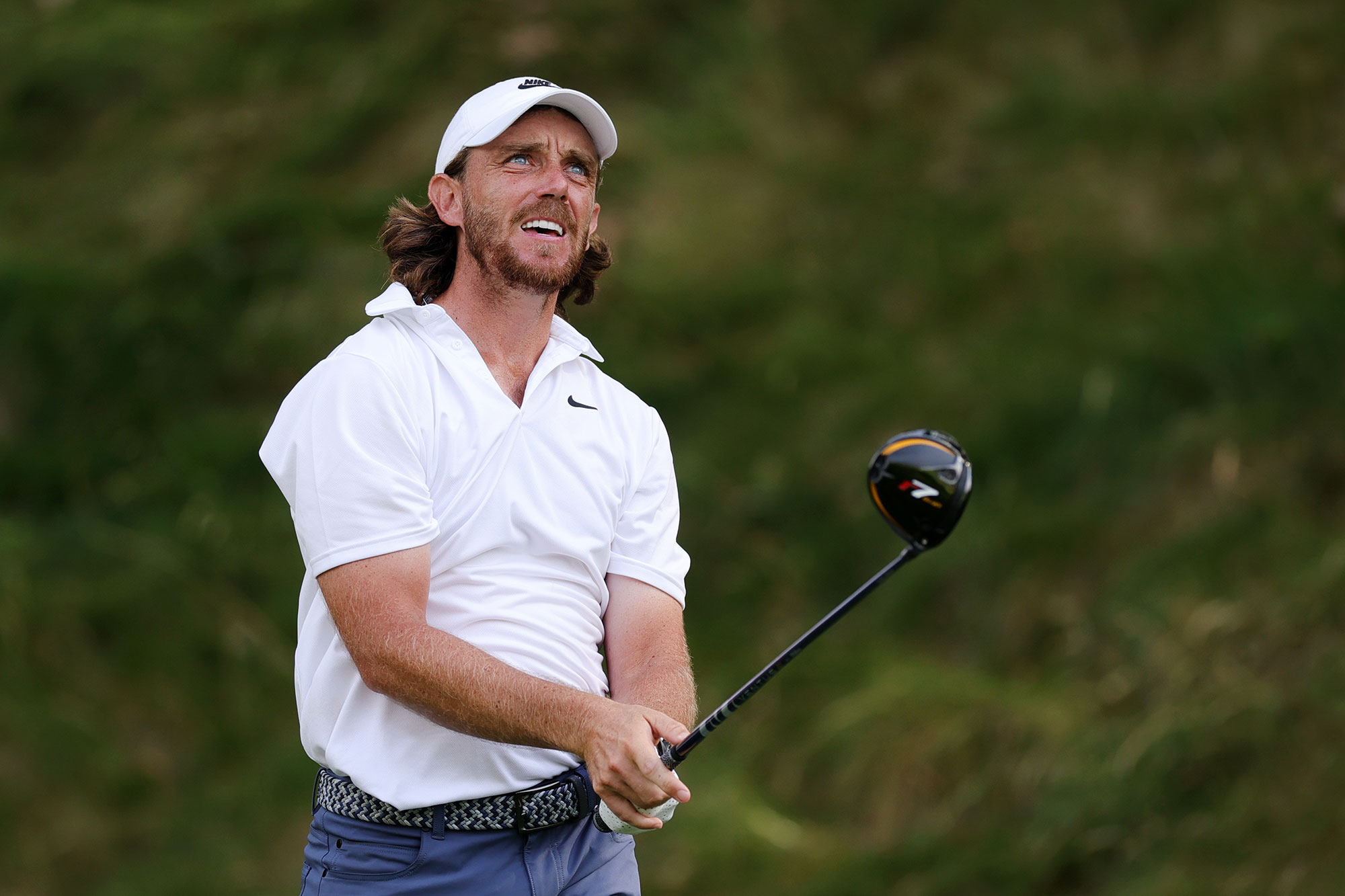 Tommy Fleetwood holding a driver towards the target after hitting a tee shot, watching the ball travel through the air