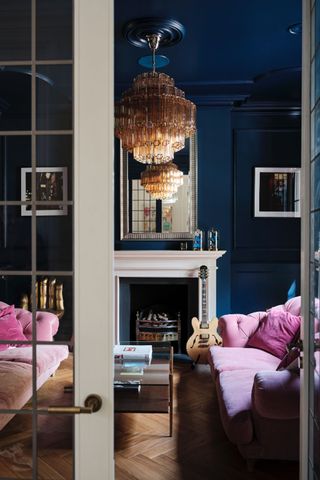 A deep blue living room with a pink sofa and a large gold chandelier