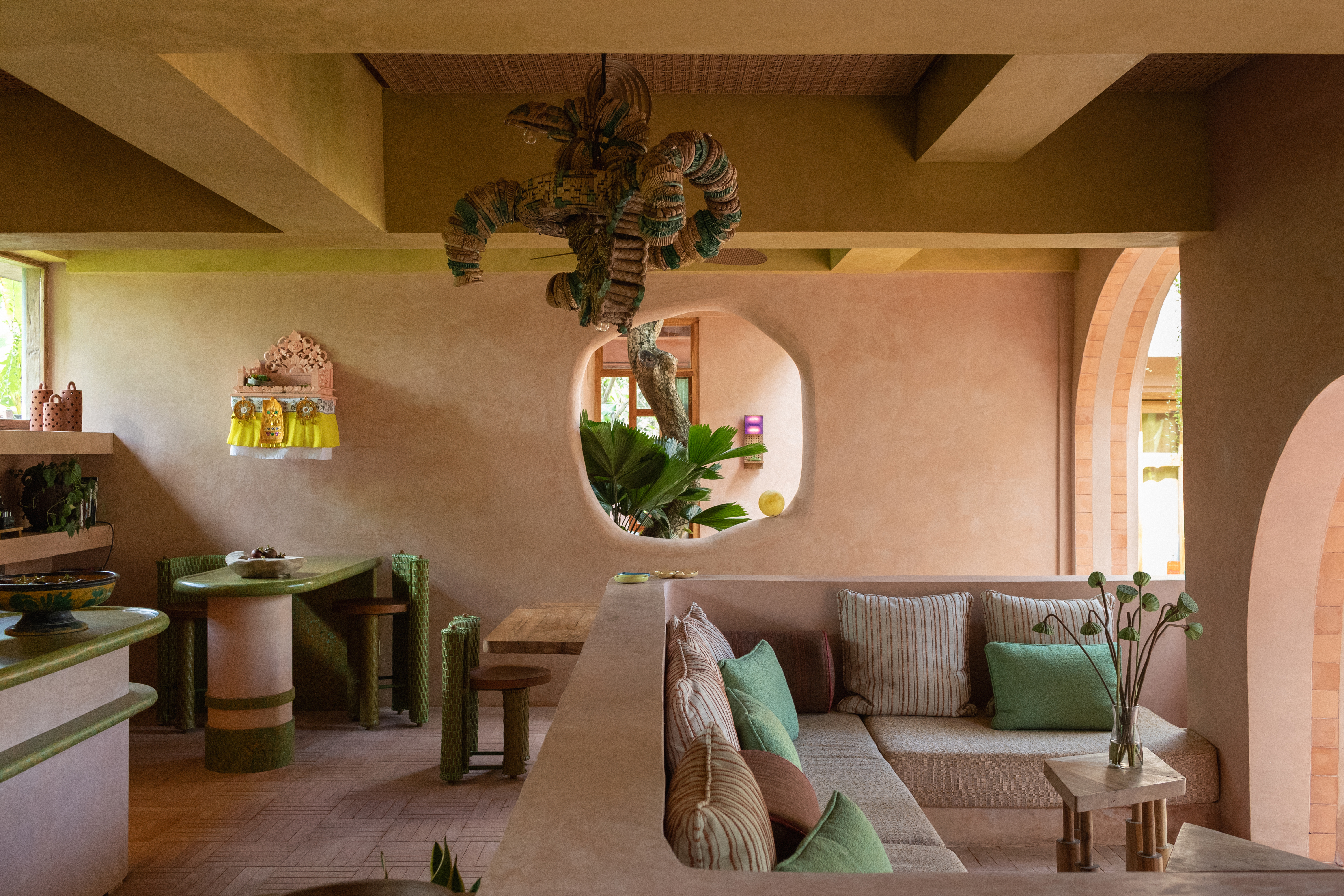 Interiors of a tropical hotel with curved passageways, terracotta walls, colorful curtains, woody furniture, color pops, and nature all around.