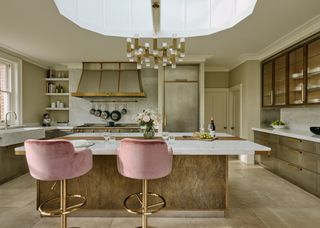 Stainless steel finishes and bright pink chairs are place by the kitchen island. A large pendant hangs above the island adding dimension to the space.