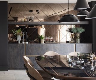 dining area with antiqued bronze glass finish above dark built in modern storage, series of black metal pendant lights above glass dining table