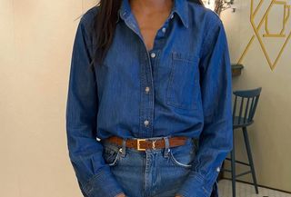 Influencer wears blue denim chambray shirt, straight-leg jeans, and Chanel bag while standing in Paris cafe.