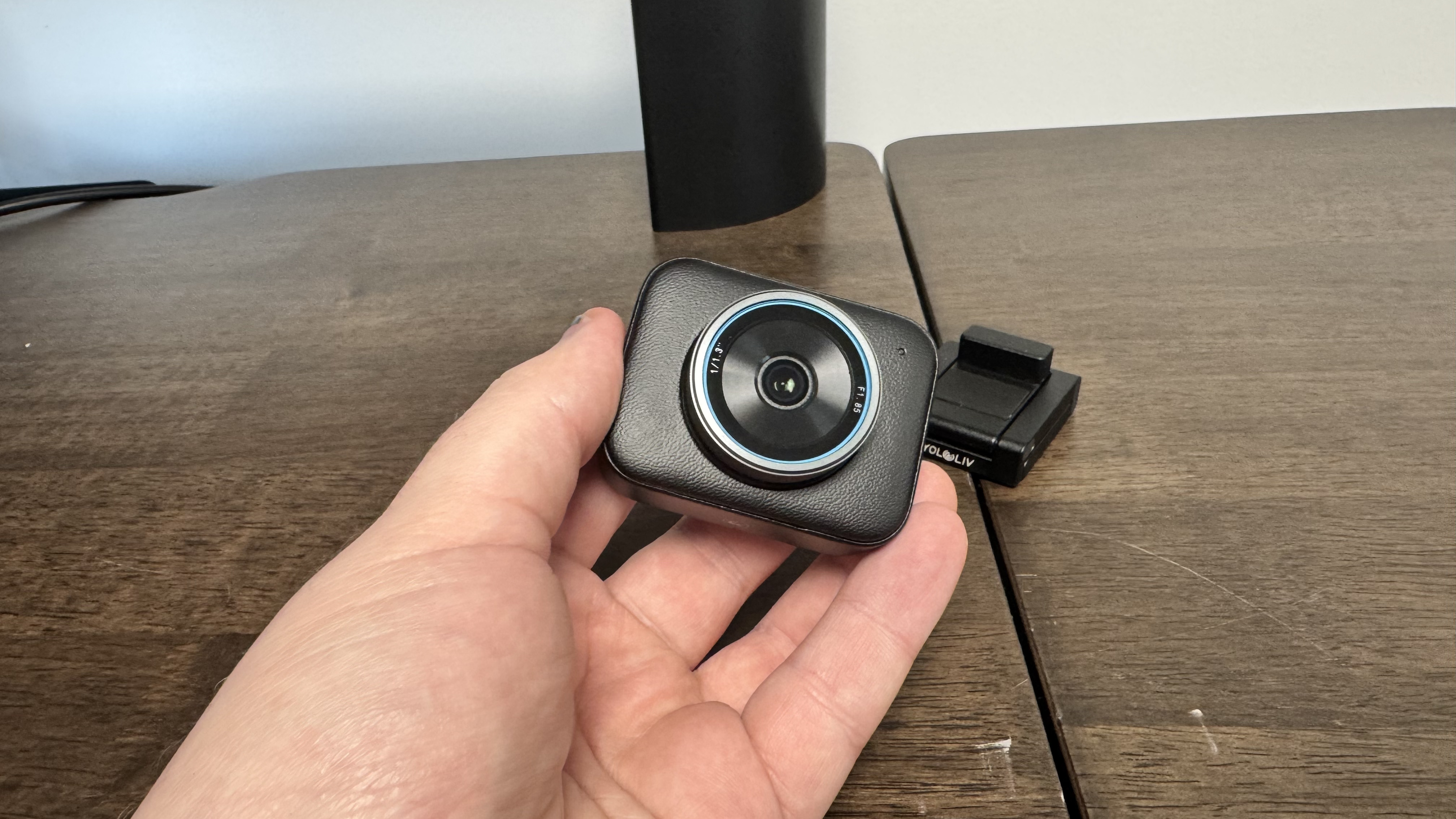 The Yololiv YoloCam S3 4K webcam in a hand, with the stand on a wooden table