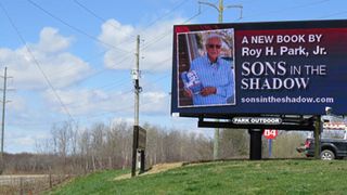 A Daktronics billboard showing a new author on the side of a rural highway.