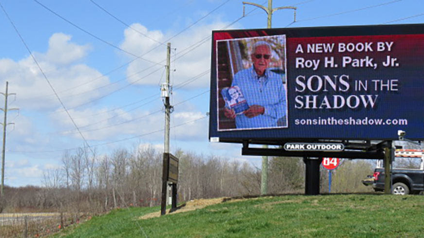 A Daktronics billboard showing a new author on the side of a rural highway. 