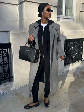 a photo of a woman wearing a long gray coat over a black hoodie with trousers and ballet flats