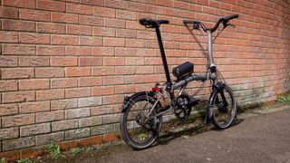 A Brompton T-Line, equipped with a Cytronex e-bike conversion kit, leans against a brick wall
