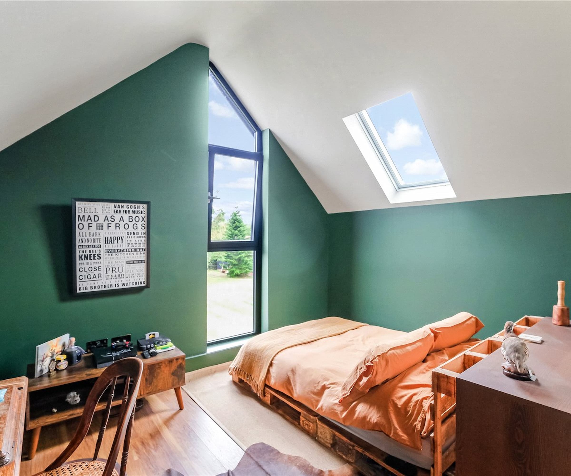 A loft bedroom with a vaulted ceiling and green walls and a dormer window