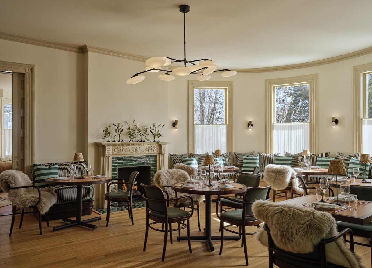 A cocooning, contemporary hotel features 1970s-inspired, plush, and puffy furniture, including upholstered modular sofas, shearling-topped chairs, and leathery chaise longue, sculptural lighting, and wooden tones mixed with vibrant greens.