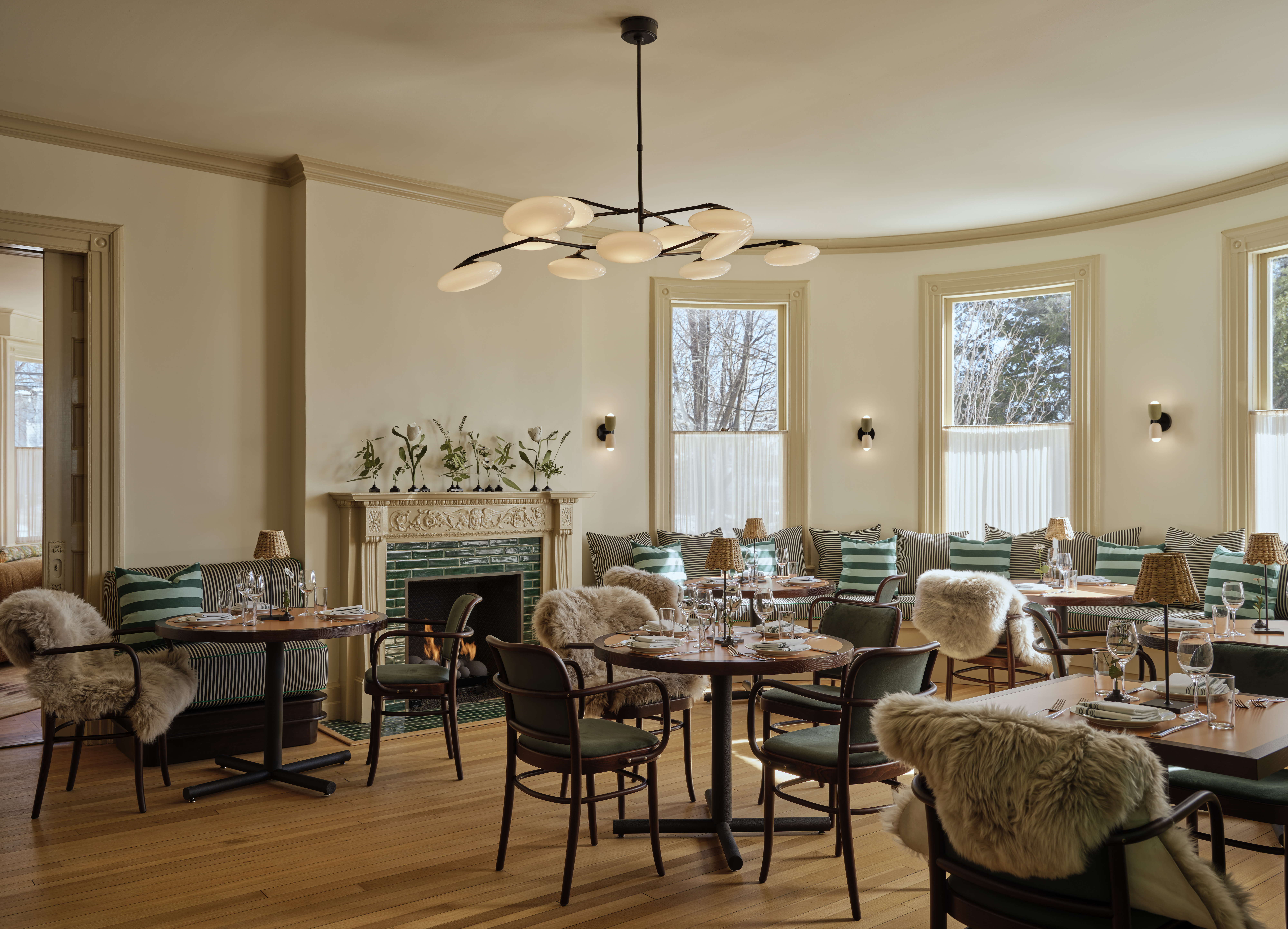 A cocooning, contemporary hotel features 1970s-inspired, plush, and puffy furniture, including upholstered modular sofas, shearling-topped chairs, and leathery chaise longue, sculptural lighting, and wooden tones mixed with vibrant greens.