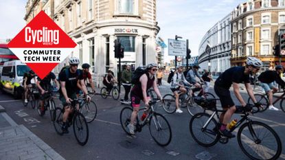 Cycling commuters queue up at traffic lights with vehicles behind in front of an HSBC bank. The Cycling Weekly Commuter Week diamond is on the left