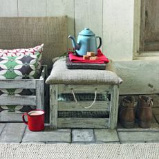An ourdoor bench made from wooden crates with a teapot on top and a tea cup next to it