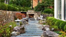 slate and gravel garden path edged with boulders and planting beds including a low hedge, and a brick wall, with an outdoor fireplace and garden furniture