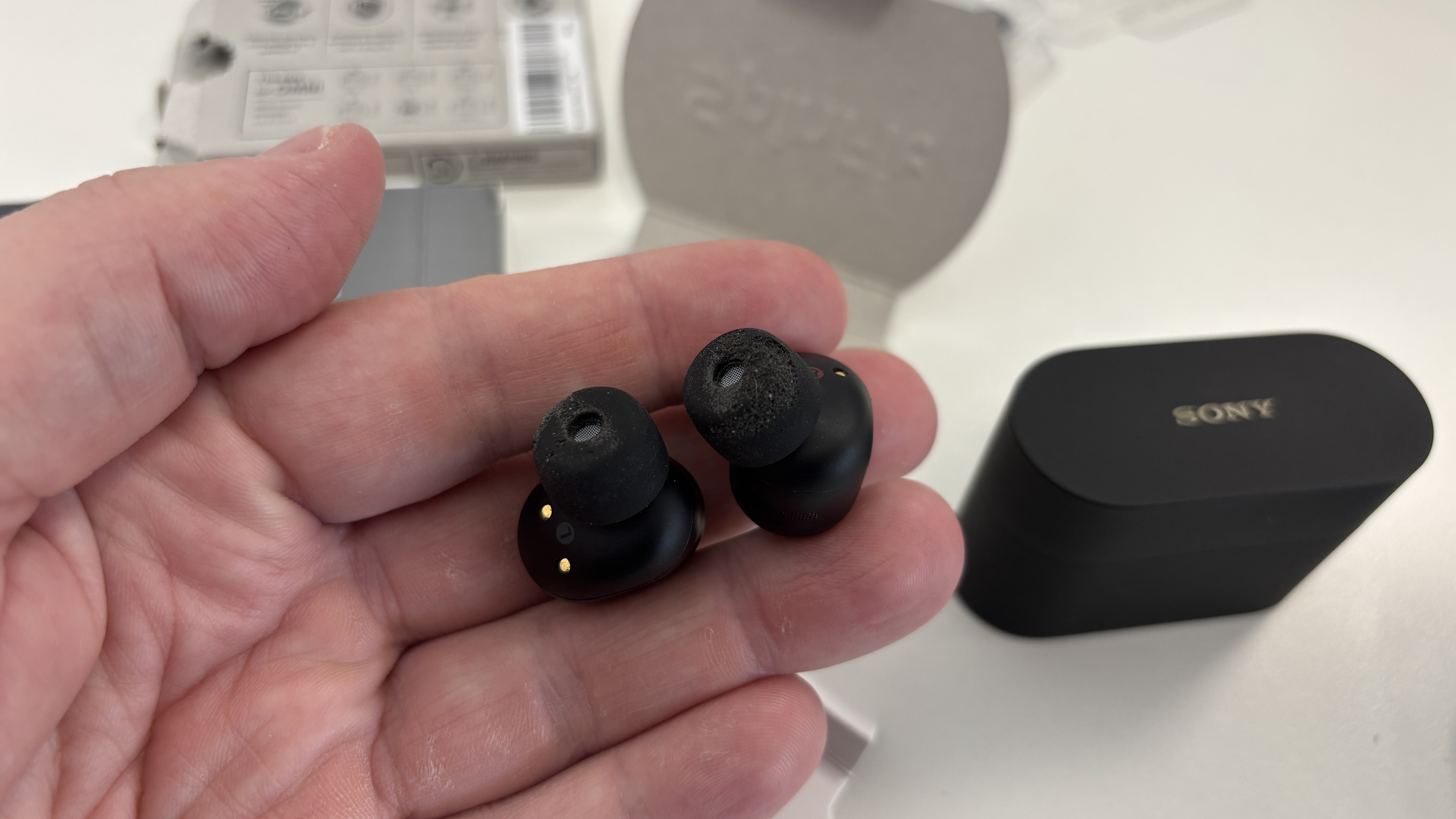 Black Sony WF-1000xM6 earbuds being held in a man's fingers