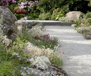 A compacted gravel pathway next to wide planting beds containing bolders