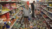 A young girl and others stands in the aisle of a grocery store with products strewn across the floor in the aftermath of an earthquake.