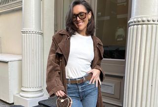 Influencer wearing white shirt, brown coat, sunglasses, and blue jeans standing on New York street.