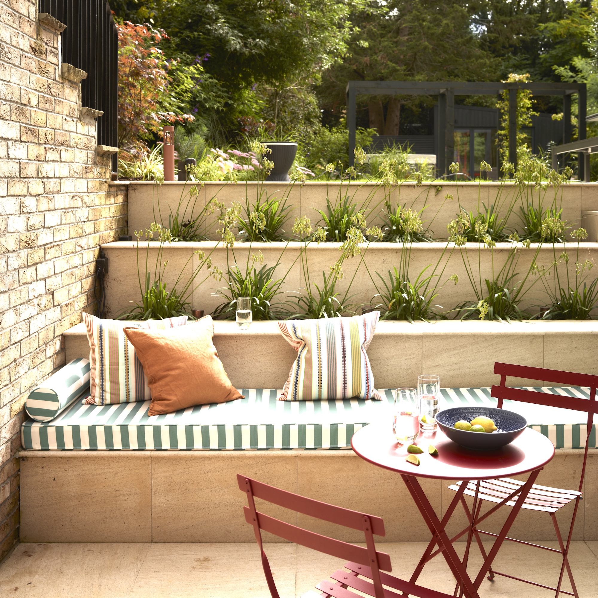 sunken courtyard garden with stepped planting and built in stone bench with striped cushions